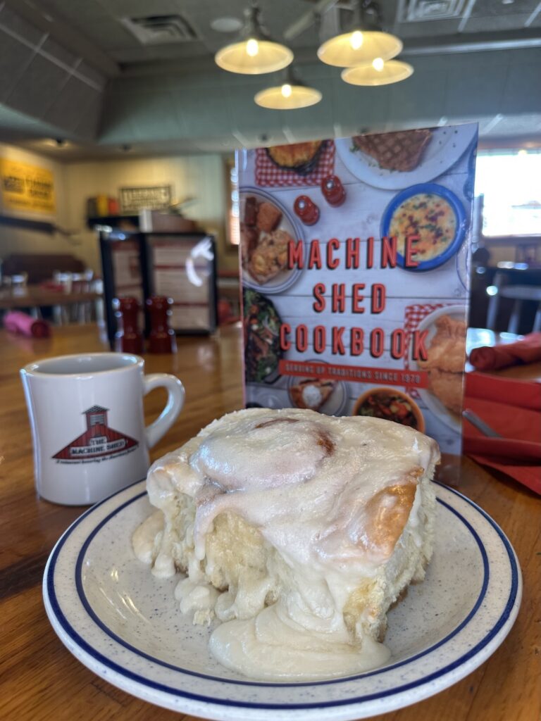 Machine Shed Cinnamon Roll with lots of frosting in front of the Machine Shed Cookbook